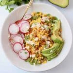 Corn, sliced radishes and avocado in a white bowl with a gold fork