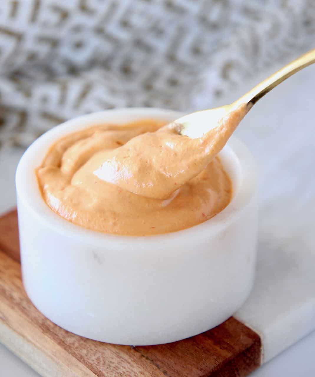 Harissa tahini sauce in white marble bowl with small gold spoon dipped in the sauce