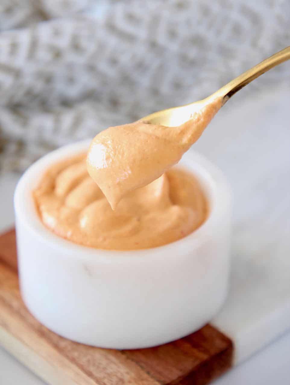 Spoon of harissa tahini sauce coming out of a bowl
