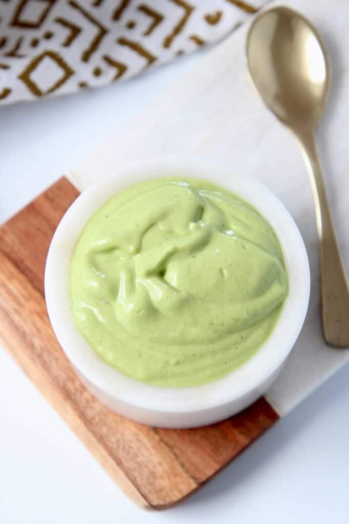 Avocado dressing in small bowl next to gold spoon