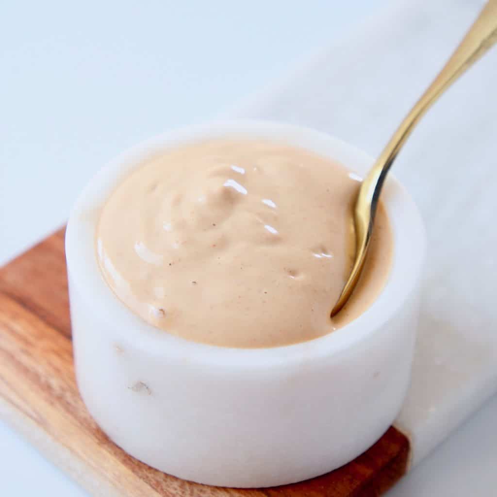 Lemon tahini dressing in white bowl with small gold spoon