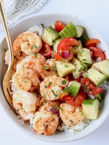 Overhead image of shrimp in bowl with tomato cucumber salad and a gold fork