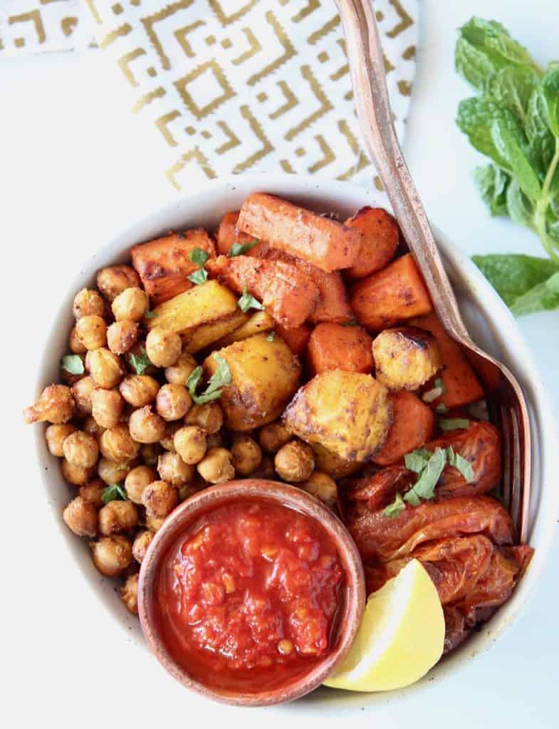 Overhead image of roasted chickpeas and carrots in a bowl with a small bowl of harissa sauce and lemon wedge