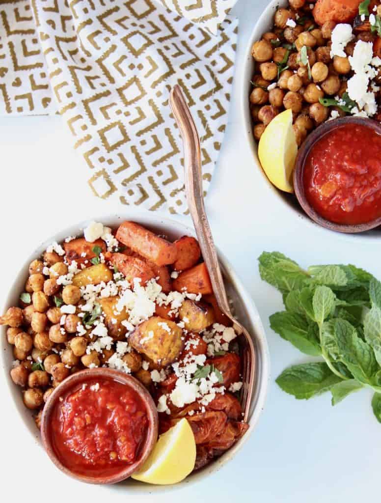 Roasted chickpeas, carrots and tomatoes in bowl, with a ramekin of harissa sauce and gold fork in the bowl