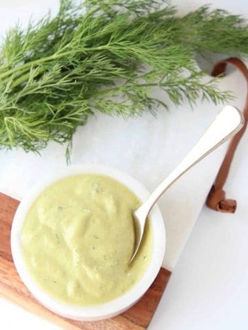 Creamy dressing in bowl with spoon next to fresh dill