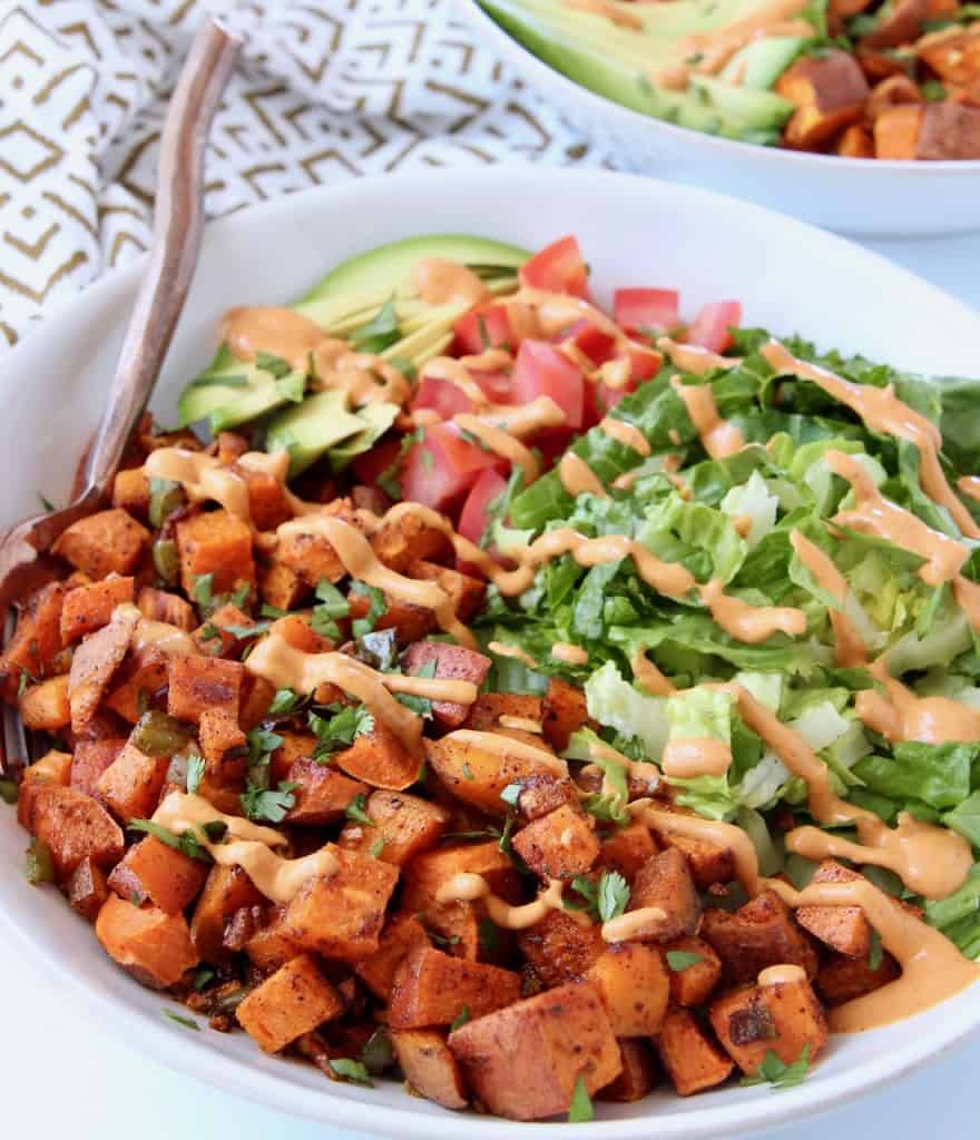 Diced roasted sweet potatoes in bowl with drizzled chipotle sauce over the potatoes