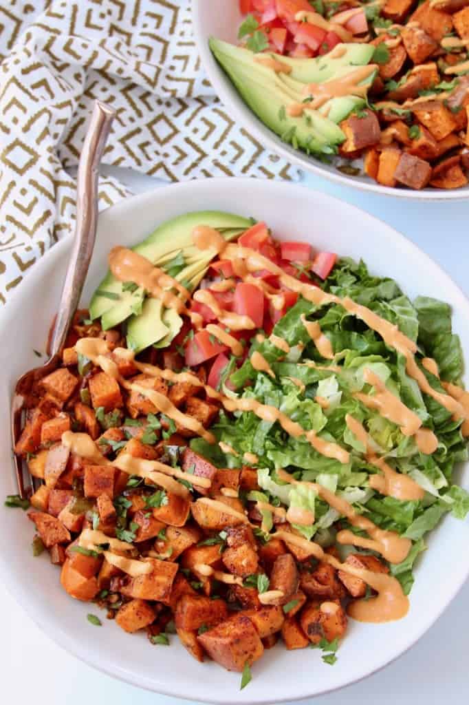 Overhead image of roasted diced sweet potatoes in bowl with lettuce, tomatoes and avocado
