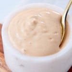 Tahini dressing in white bowl with small gold spoon