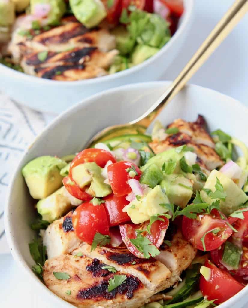 Sliced grilled chicken in bowl topped with avocado salsa