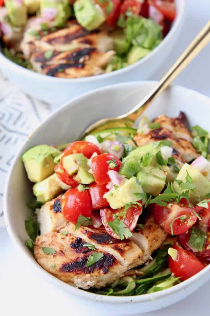 Sliced grilled chicken in bowl topped with diced avocado salsa