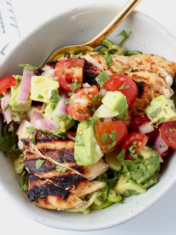 Sliced chicken in bowl topped with avocado tomato salsa