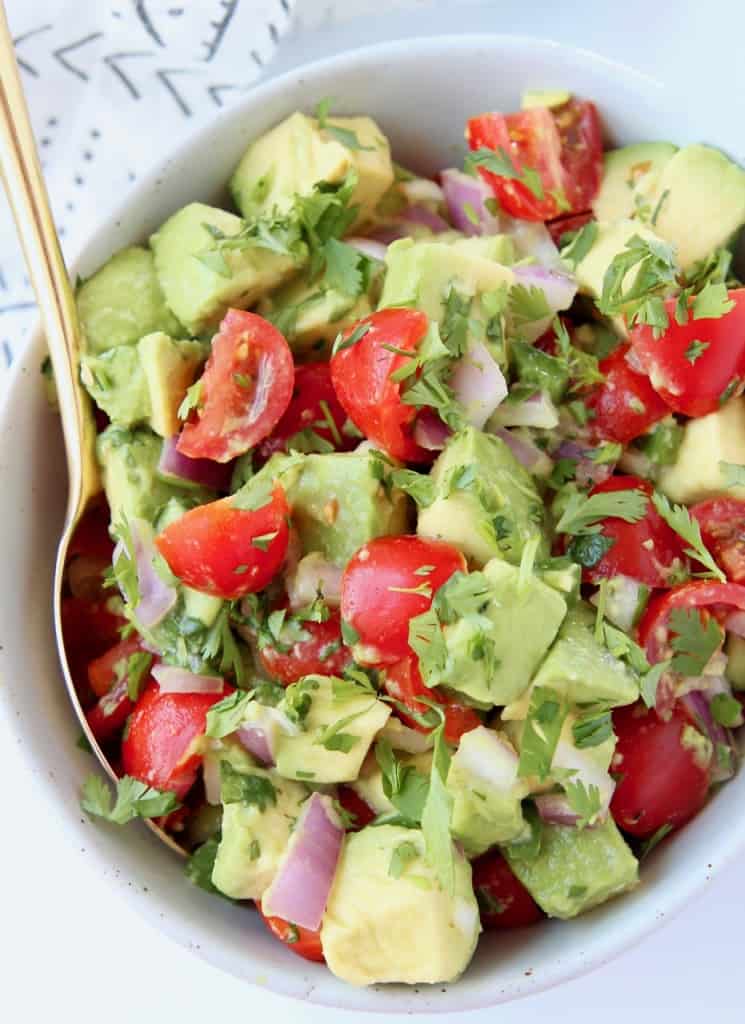 Avocado and tomato salsa in bowl with gold spoon
