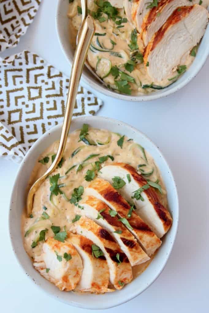 Overhead image of sliced chicken bread on top of cheesy zucchini noodles in bowl