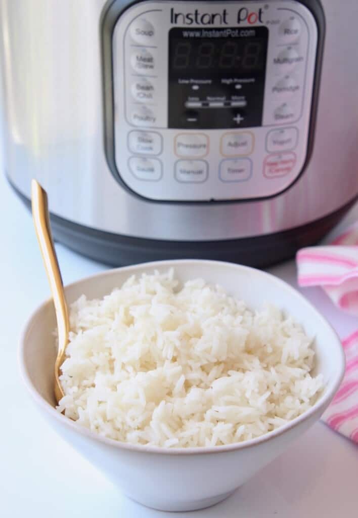 White rice in bowl with gold spoon, sitting in front of an instant pot