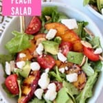 Salad in bowl topped with grilled peach slices and feta cheese