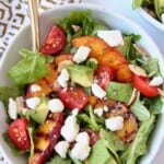 Salad in bowl topped with grilled peach slices and feta cheese