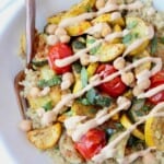 Roasted vegetables in bowl with quinoa, drizzled with tahini dressing