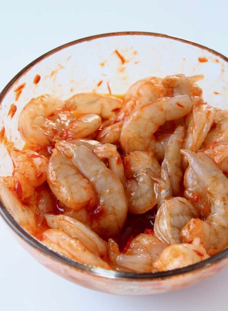 raw shrimp tossed with harissa sauce in glass bowl
