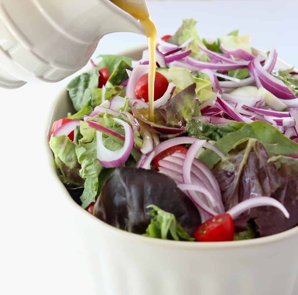 vinaigrette dressing being poured onto a salad in a large bowl