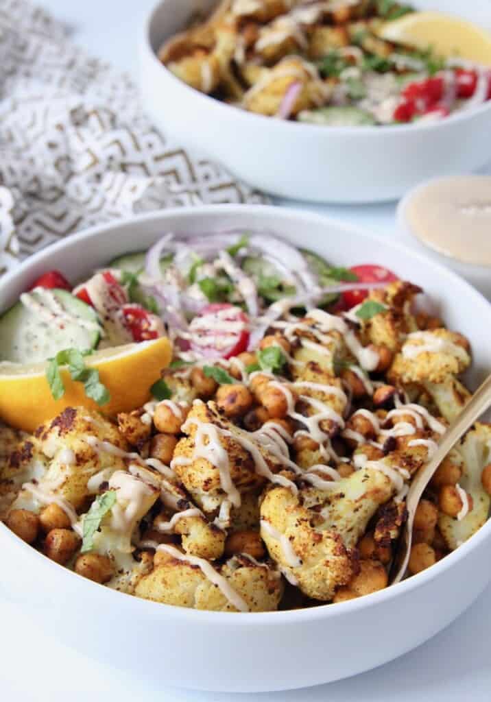 white bowl filled with roasted cauliflower shawarma, veggies and a gold fork