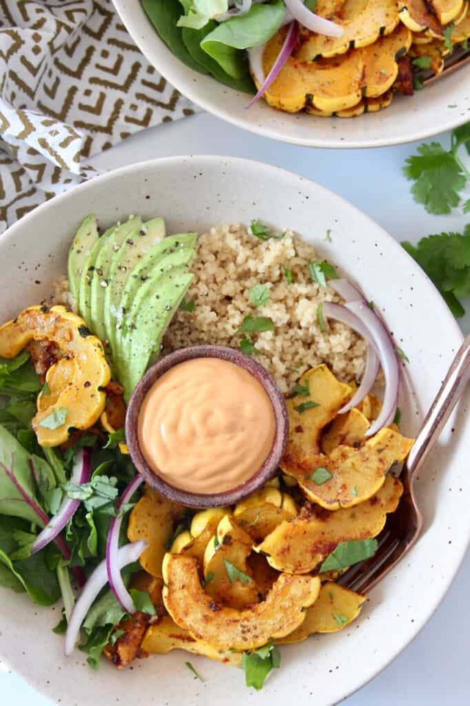 overhead image of roasted delicata squash in bowl with quinoa, avocado and greens