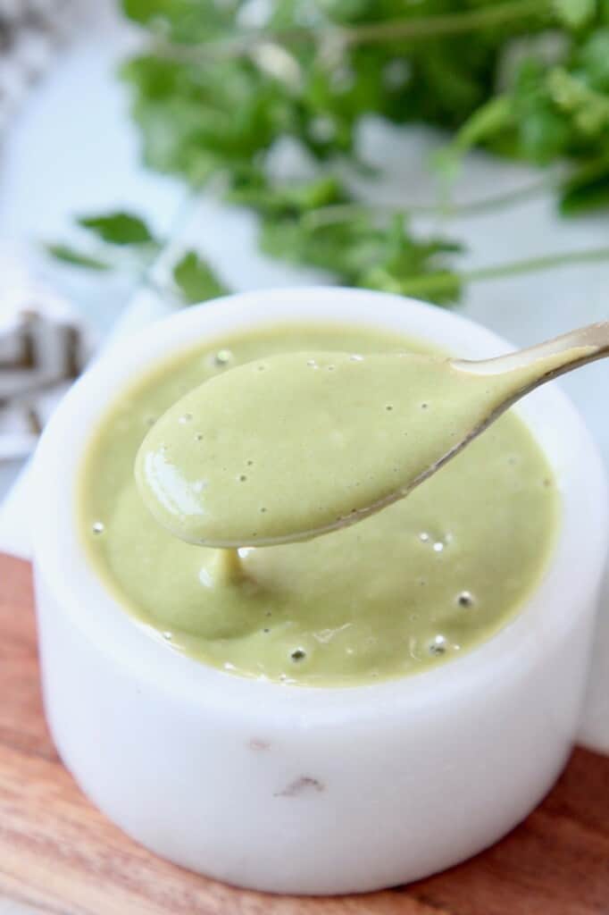 small spoon scooping salad dressing out of white bowl