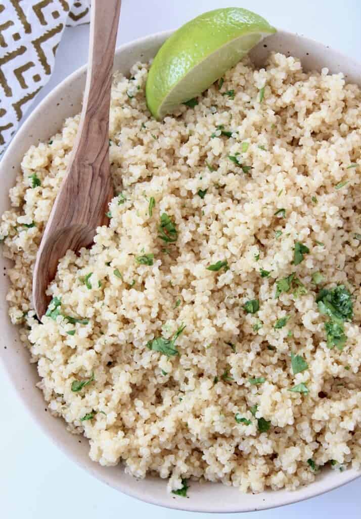 cooked quinoa tossed with cilantro in bowl with spoon and lime wedge