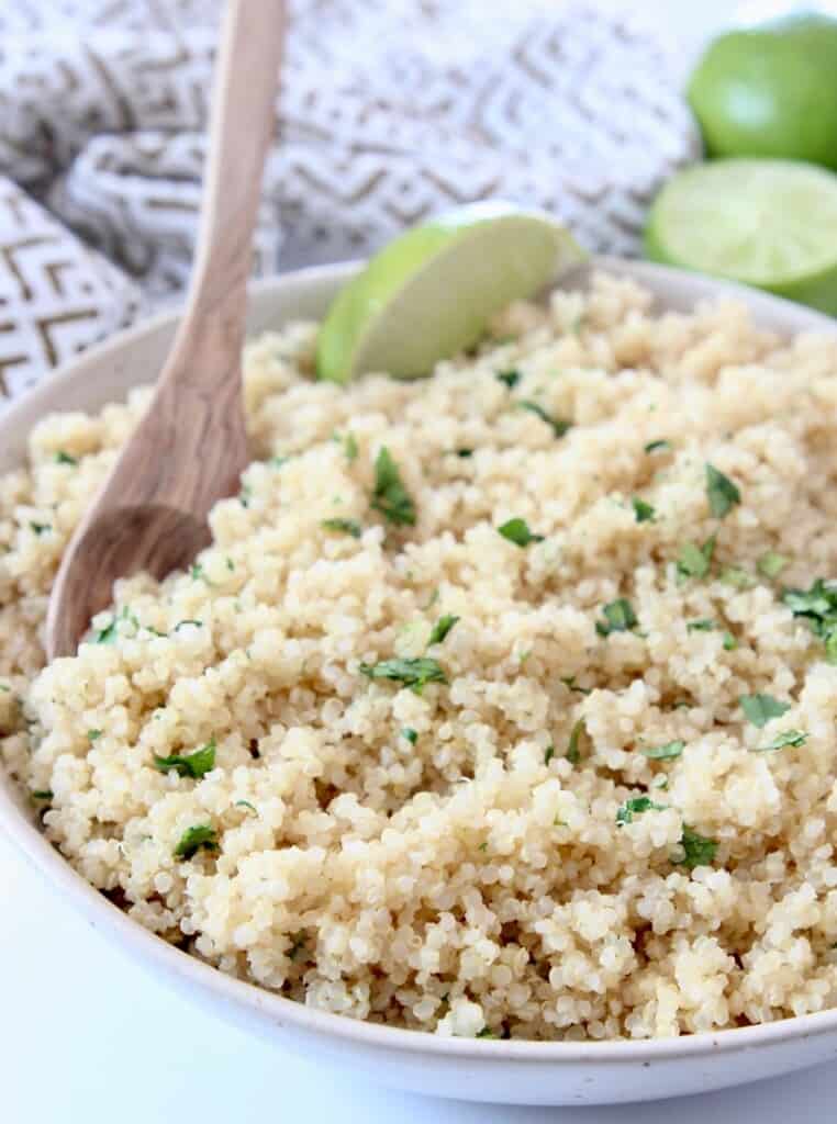 cooked quinoa in bowl with wooden spoon and lime wedge