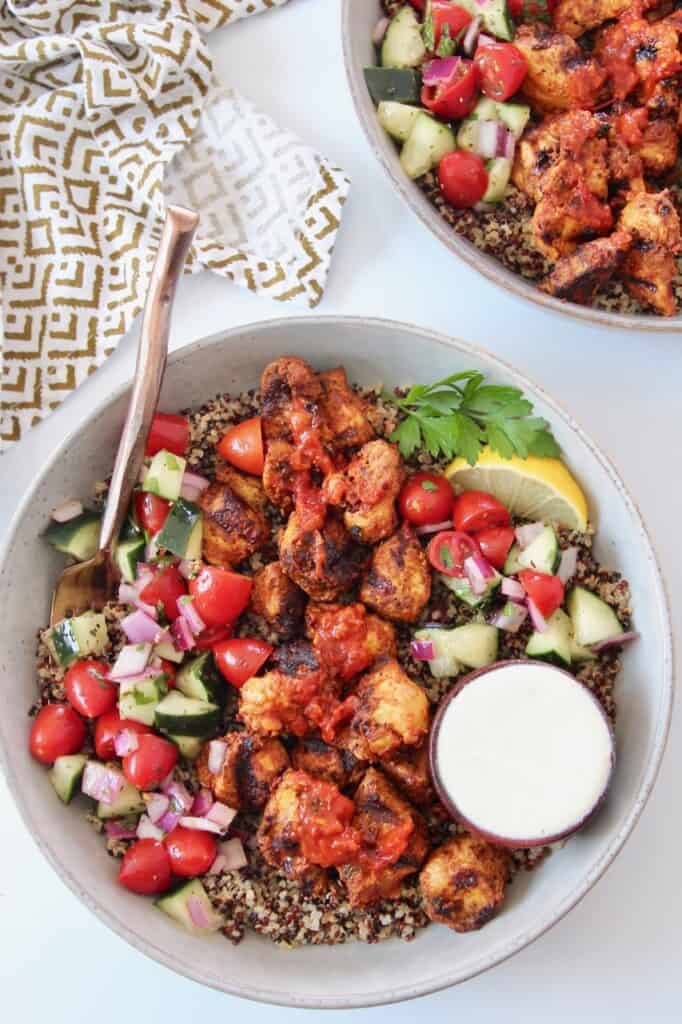 grilled cubes of harissa chicken in bowl with tomato cucumber salad