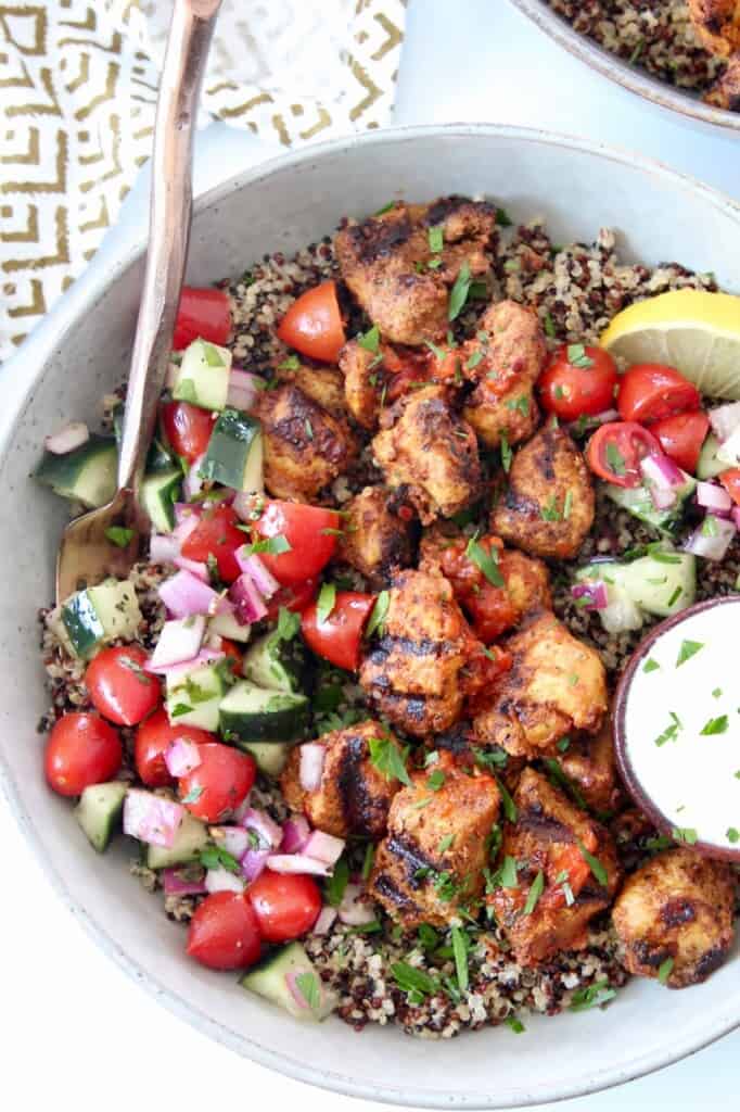 grilled pieces of harissa chicken in bowl with cucumber tomato salad and quinoa