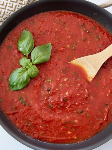 marinara sauce in pan with spoon and fresh basil leaves