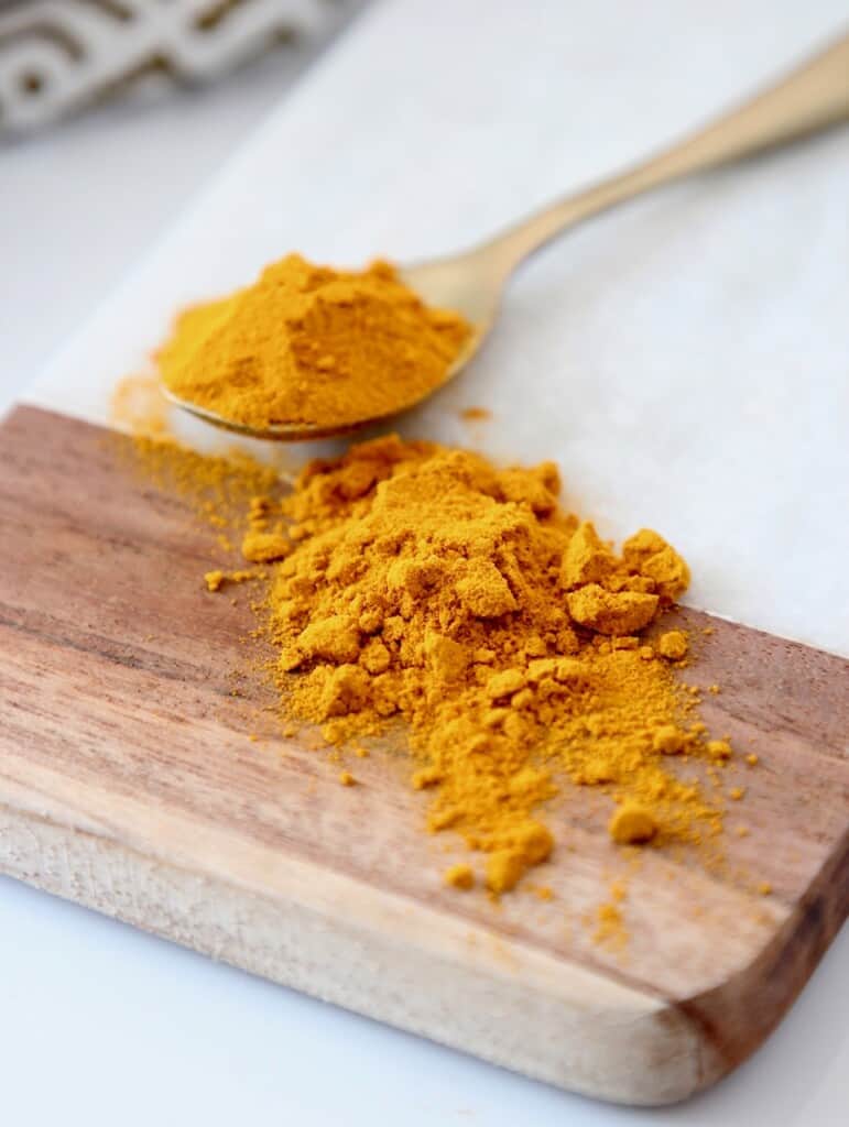 ground turmeric in spoon and on marble and wood cutting board