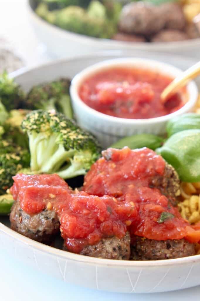 vegan meatballs covered in marinara sauce in bowl with broccoli