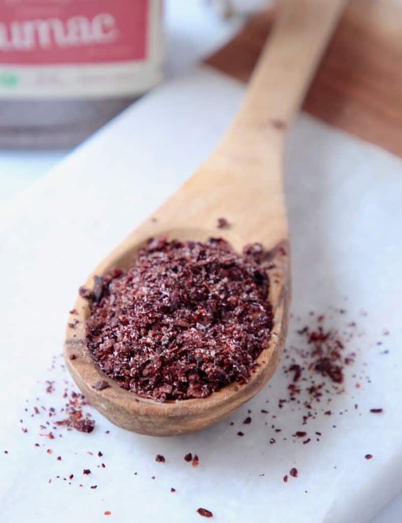 sumac spice in wooden spoon on marble cutting board