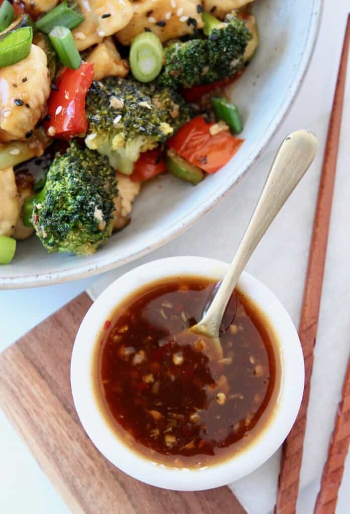 teriyaki sauce in bowl with spoon next to a bowl of teriyaki chicken with vegetables