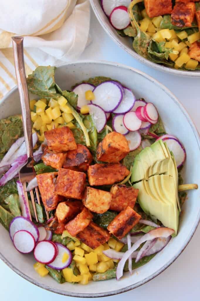 cubes of cooked buffalo tempeh on top of salad in bowl