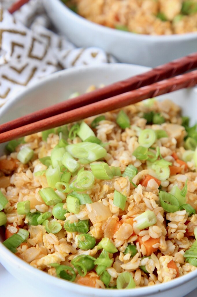 fried rice in white bowl with brown chopsticks on the side
