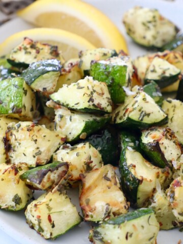 cooked cubes of zucchini on plate with lemon wedges