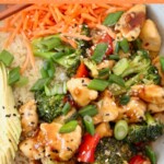 cooked teriyaki chicken and vegetables in bowl with diced green onions and shredded carrots