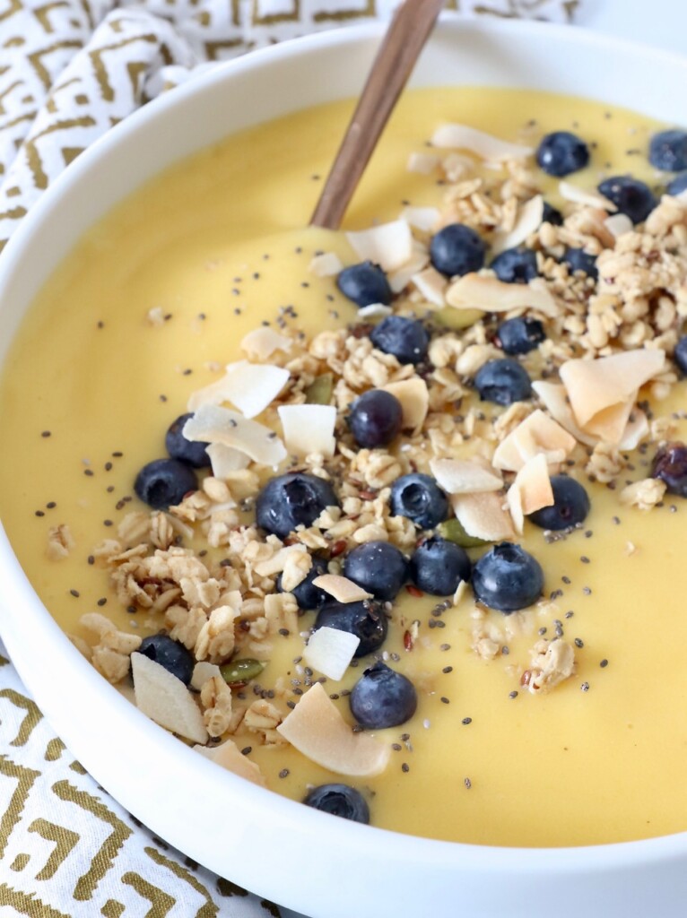 mango smoothie in bowl topped with granola and blueberries