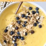 mango smoothie in bowl with granola, coconut and blueberries on top