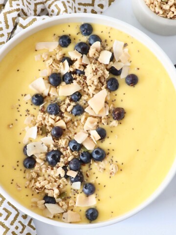 mango smoothie bowl topped with granola, coconut and blueberries