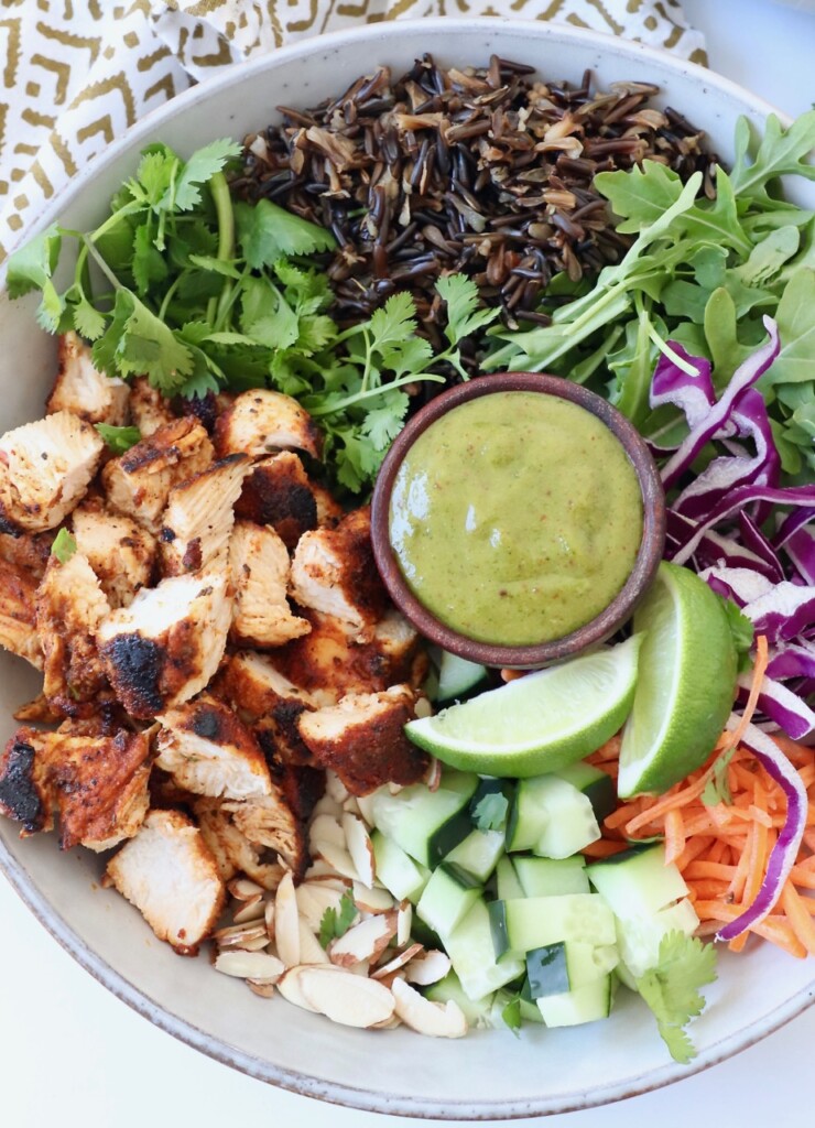 blackened chicken, wild rice and vegetables in bowl with ramekin of spicy cilantro sauce