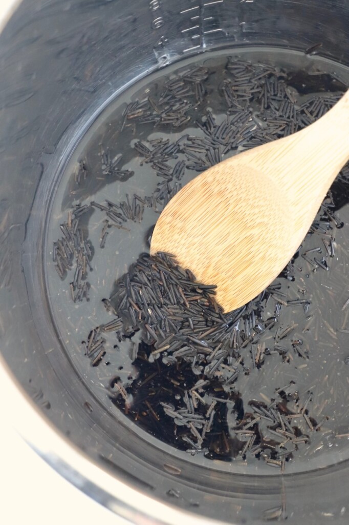 uncooked wild rice in instant pot with water and wooden spoon
