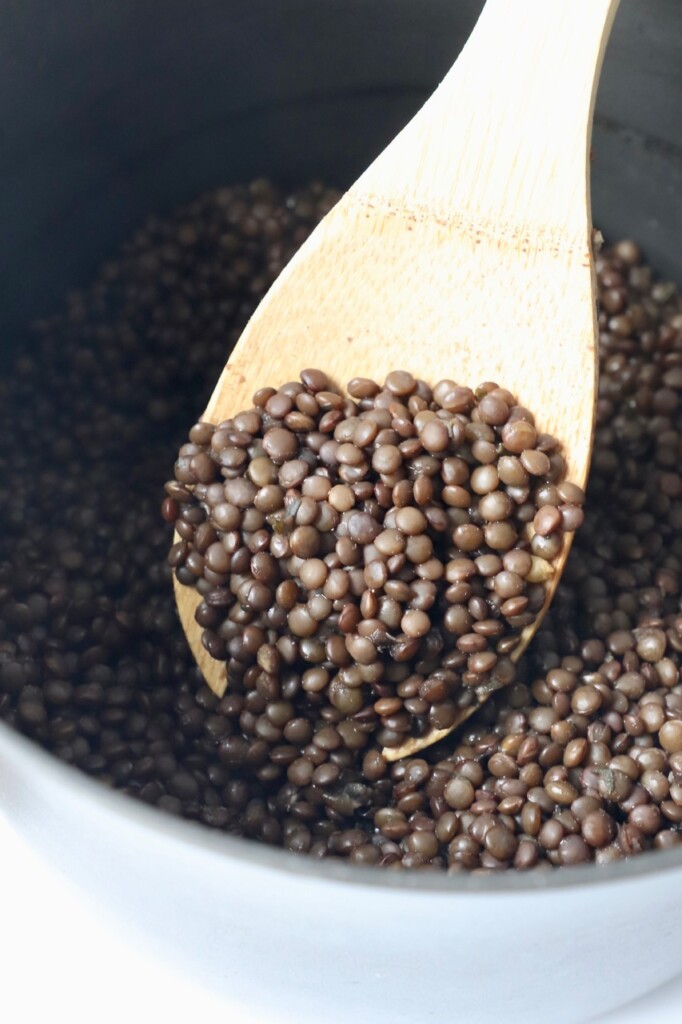 black lentils in wooden spoon in saucepan