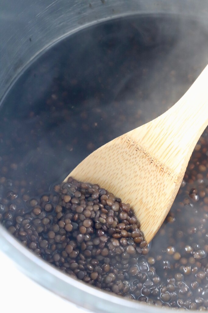 black lentils cooked in Instant Pot with wooden spoon in pot