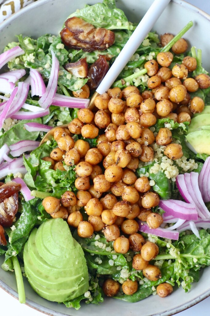 roasted chickpeas on top of salad with sliced onions and avocado