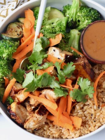 brown rice, vegetables, chicken and peanut sauce in bowl with fork