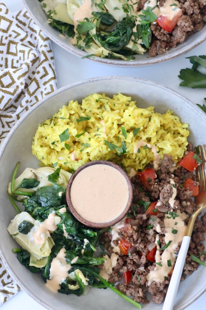 cooked ground beef, lemon rice, veggies and tahini sauce in bowl