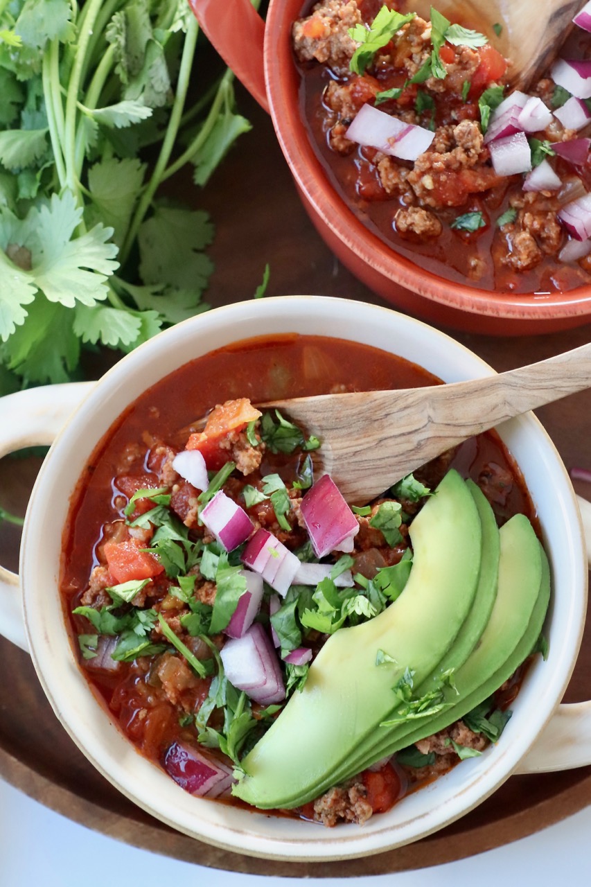 chili in bowls with cilantro, onion and avocado on top